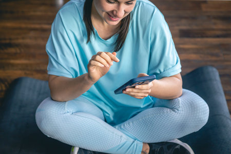 A woman sits on a mat and uses a smartphone, online workout concept.