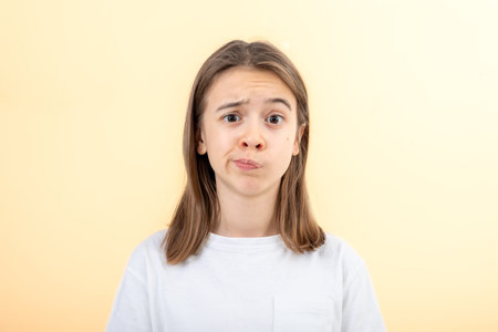 A teenage girl grimaces with displeasure on a white background, isolated.