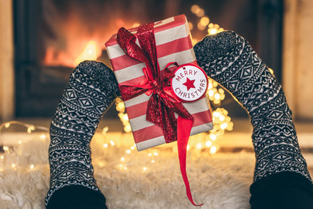 Christmas present is held by feet on the background of the fireplace.の写真素材