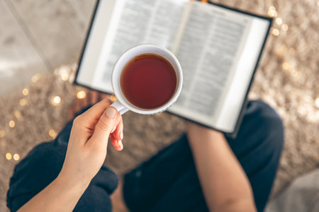 Top view, woman holding mug of tea while reading a book on the floor.の写真素材