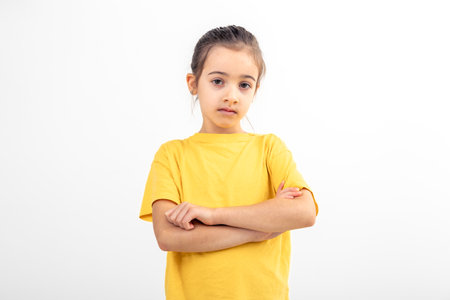 Sad school girl dressed yellow t-shirt arms folded on white background.の写真素材