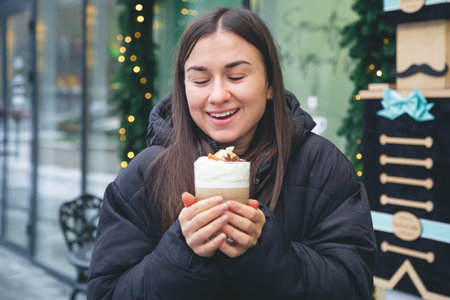 A young woman drinks coffee with cinnamon and anise in a cafe outside.の写真素材