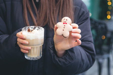 A young woman drinks coffee with a gingerbread boy in a cafe on the street.