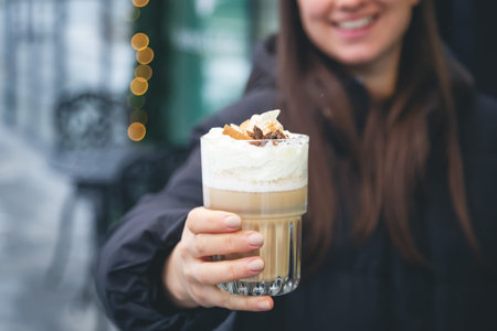 Coffee with cream, cinnamon and star anise in female hands outside.