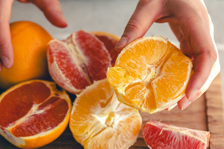 Peeled oranges in female hands and on a wooden cutting board for juice.の写真素材