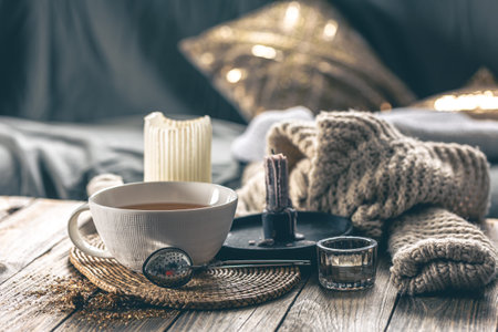 Cozy home composition with a cup of tea, candles and a knitted element.