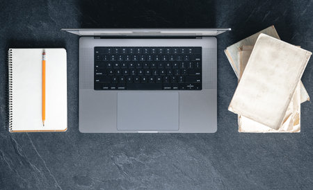 Laptop, books and notepad on a dark textured background, top view.