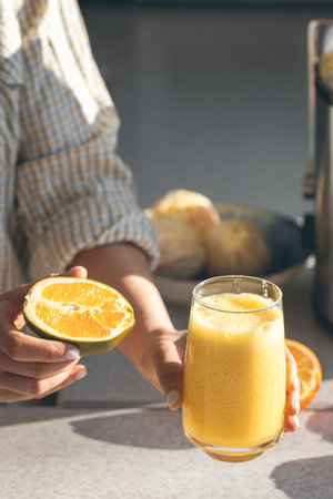 A glass of freshly squeezed orange juice and half an orange in female hands.の写真素材