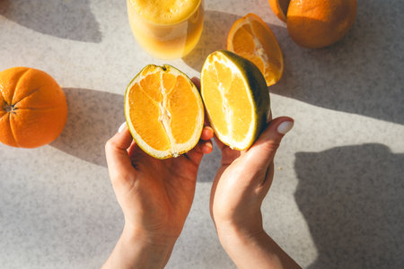 Halves of a fresh orange in female hands on the background of the kitchen table.の写真素材