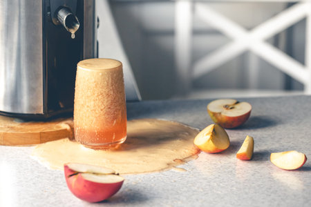 Juicer and glass filled with apple juice on the kitchen table.の写真素材