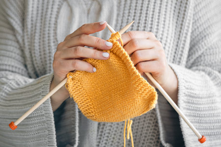 Close-up of female hands knitting yellow wool sweater.