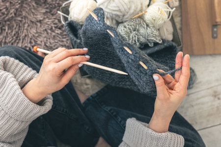 Close-up of female hands knitting grey wool sweater, top view.