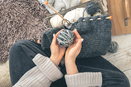 A woman with threads knits while sitting on the floor at home, top view.
