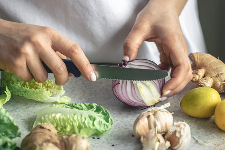 A woman cuts onions for salad on the kitchen table, close-up.