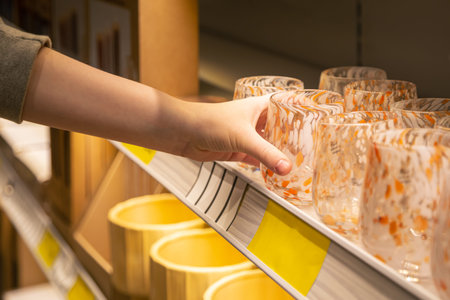 Woman holding glass from a shelf in homeware store.
