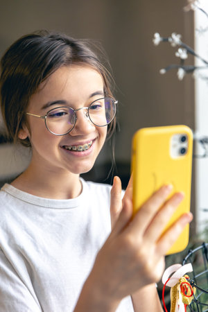A teenage girl in glasses and braces communicates via video call.