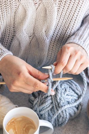 A woman knits with gray thread, close-up.