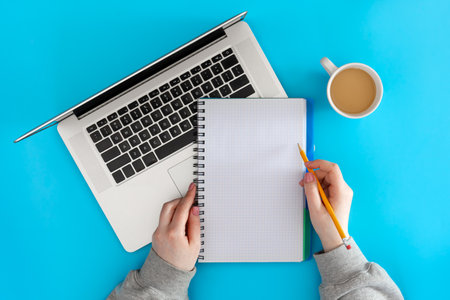 A blank notepad in the hands of a female student, a laptop and a cup of coffee.の写真素材