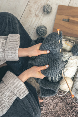 Close-up of female hands knitting grey wool sweater, top view.