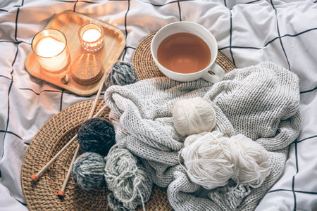 Cozy composition with a cup of tea, a candle and knitted elements on a blanket.