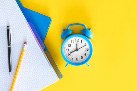 Blue alarm clock and notepads on a yellow background, flat design.