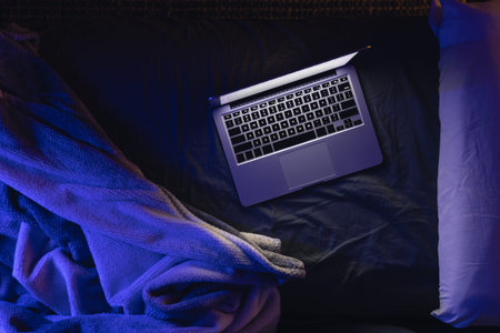 Laptop with glowing screen on bed at night, top view, copy space.