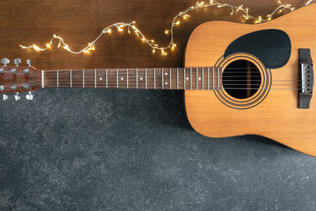 Acoustic guitar and garland on a textured black and wooden background, top view.の写真素材