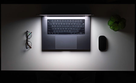 Laptop, computer mouse and glasses on a white table at night, top view.