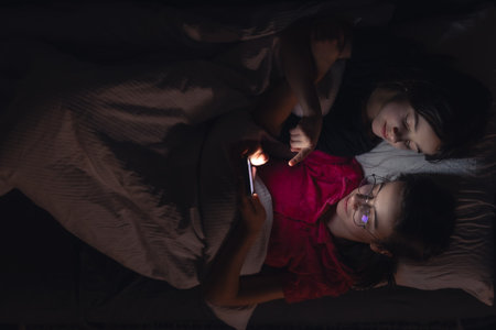 Teenage girls with a smartphone lies in bed at night, top view.の写真素材