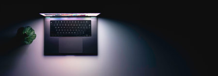 Laptop with a glowing screen on a table in the dark, top view, copy space.