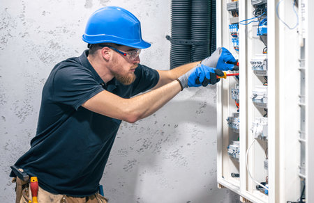 A male electrician works in a switchboard with an electrical connecting cable.