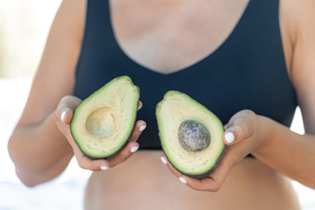 Pregnant woman holding avocado, health and maternity concept.