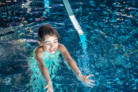 A young teenager girl in a swimsuit, swimming in a blue pool.の写真素材