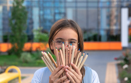 Schoolgirl with pencils in hands close-up. Student with school supplies on school background. Smilesの写真素材