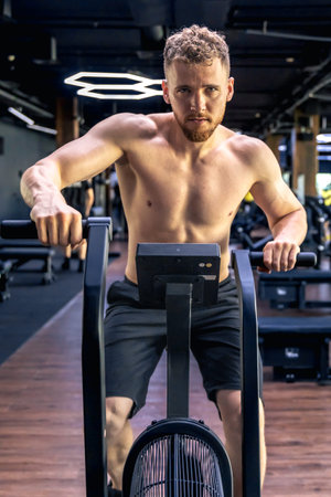 Exercises on an air bike in full height. Young athlete in the gym.