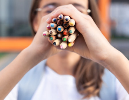 Schoolgirl with pencils in hands close-up. Student with school supplies on school background. Smilesの写真素材