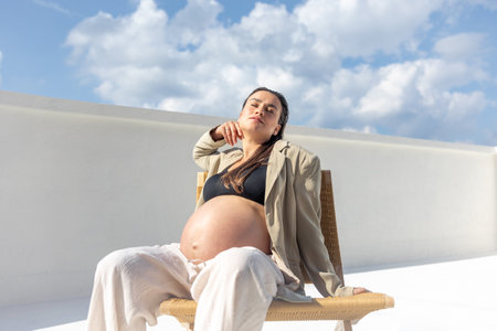 Stylish pregnant woman on a beautiful wicker chair. On a light background.の写真素材