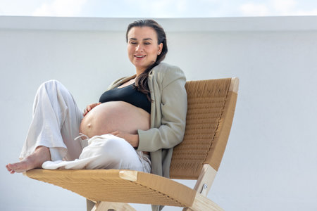 Stylish pregnant woman on a beautiful wicker chair. On a light background.の写真素材