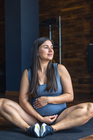 Pregnant woman in the gym doing warm-up. Sitting on a yoga mat.の写真素材
