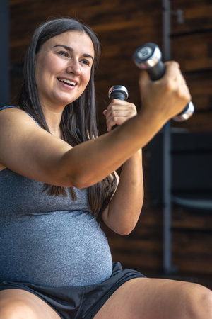 Pregnant woman in the gym with dumbbells in her hands.の写真素材