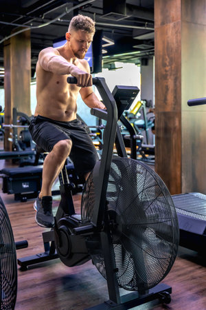 Exercises on an air bike in full height. Young athlete in the gym.の写真素材