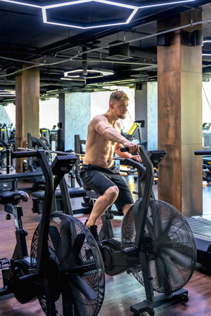 Exercises on an air bike in full height. Young athlete in the gym.の写真素材