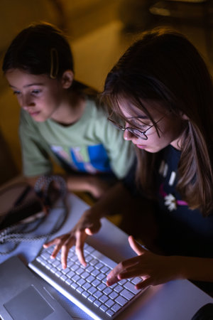 Two young girls at the computer at night.の写真素材