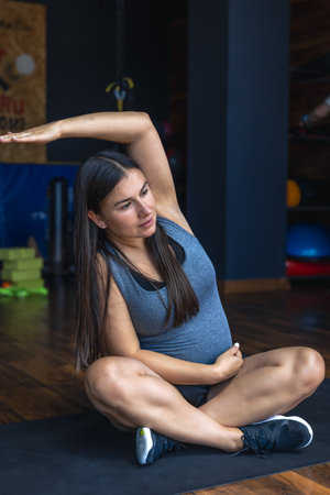 Pregnant woman in the gym doing warm-up. Sitting on a yoga mat.の写真素材