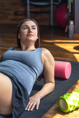 Pregnant woman in the gym on a mat with a massage roller.の写真素材