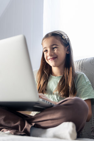 A schoolgirl studies online at home. The girl is typing on the laptop keyboard.の写真素材