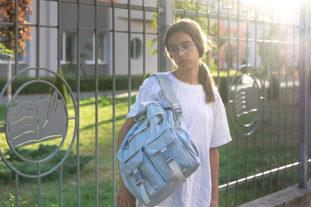 Upset schoolgirl with backpack near school. Sunset in the background. Upset girl.