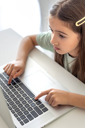A schoolgirl studies online at home. The girl is typing on the laptop keyboard.の写真素材