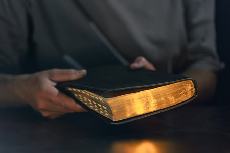 A man holds a Bible in his hands. Bible with golden pages.の写真素材
