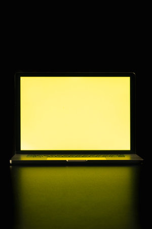 Modern laptop with blank yellow screen isolated on black background. Close up.